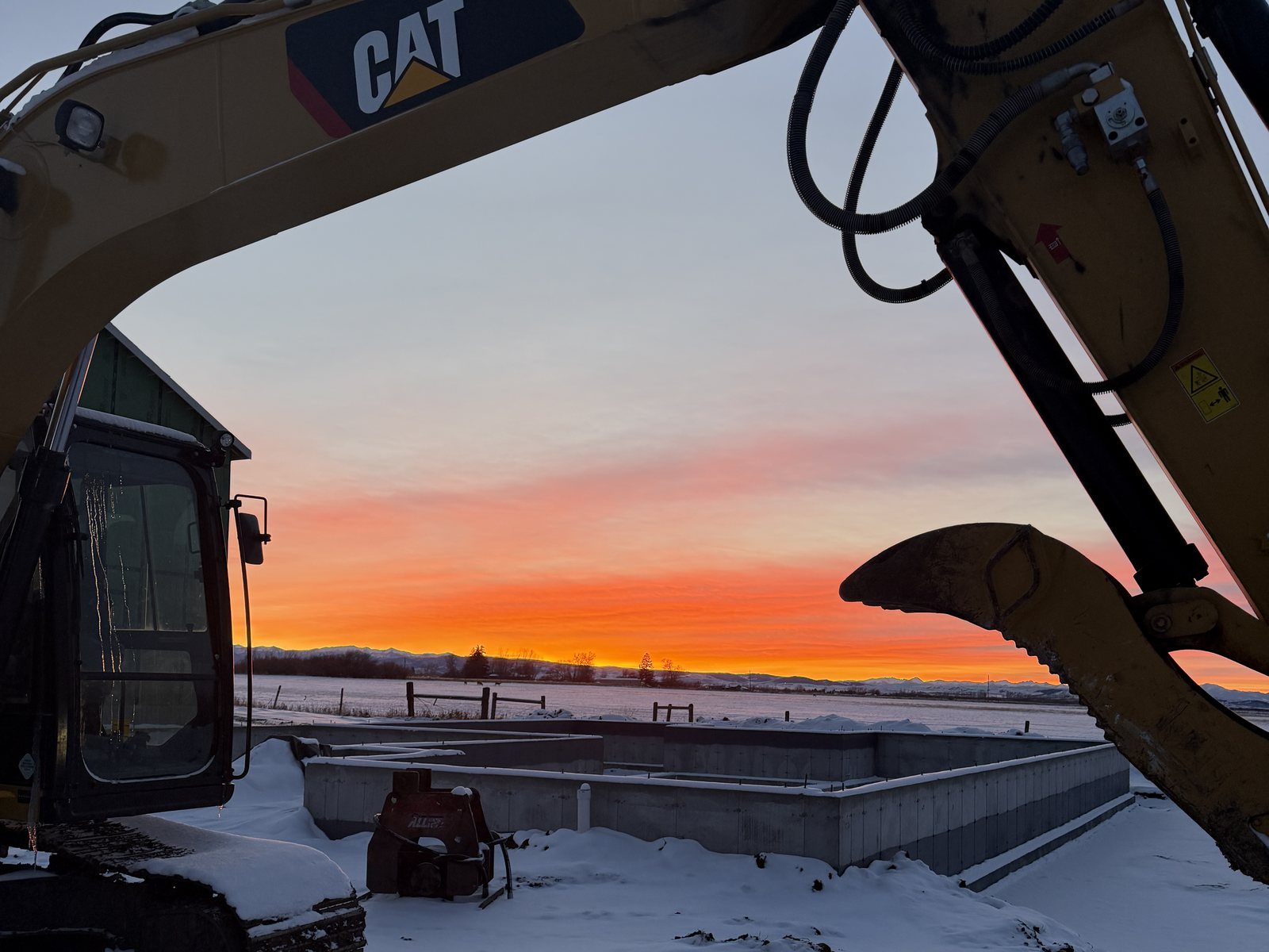 Excavator boom framing sunrise over a formed foundation — Site No. 004